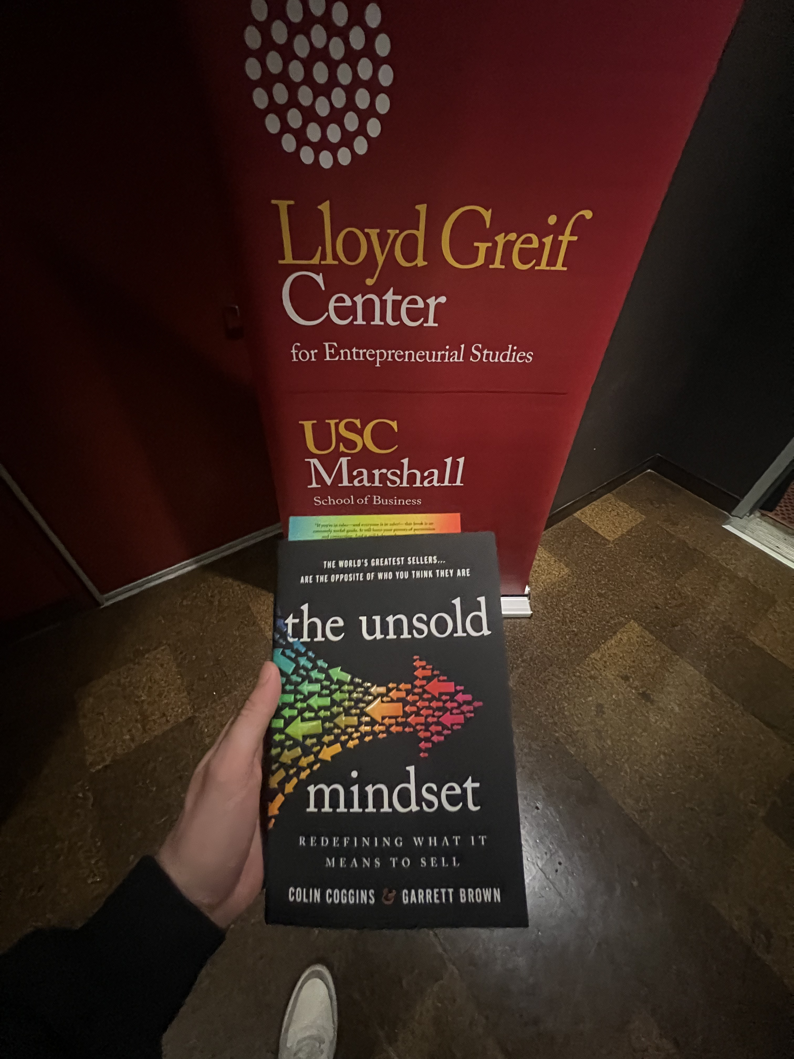 Wide angle shot of The Unsold Mindset book held in front of the USC Marshall Lloyd Greif Center sign